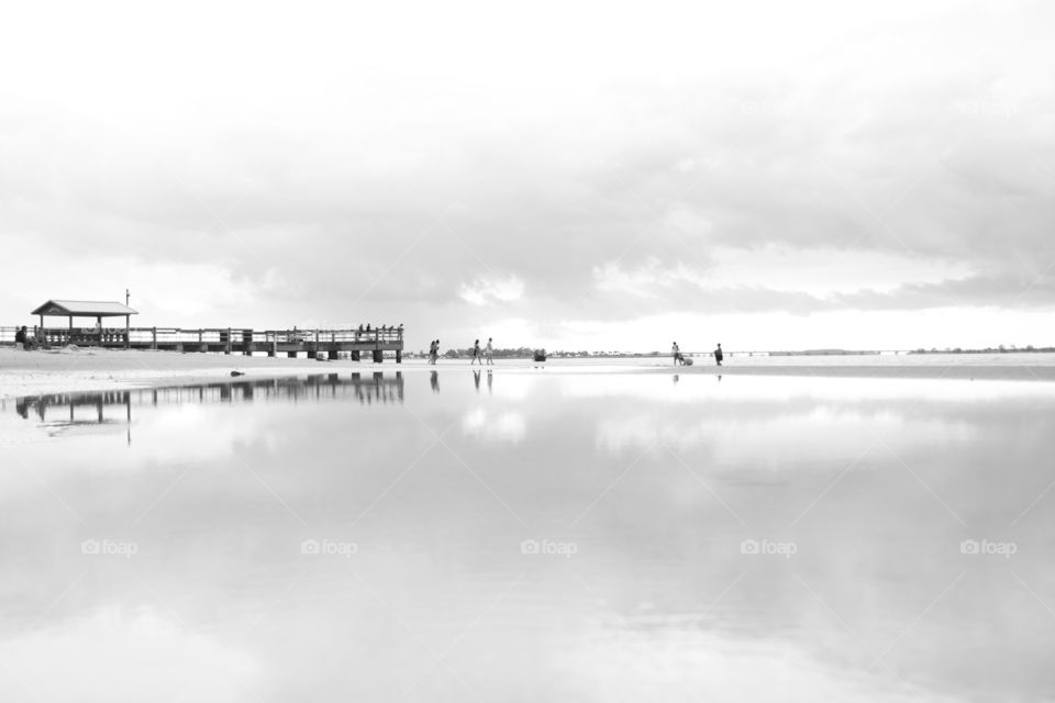 Black and white silhouette of reflective beach and pier in summer with people 