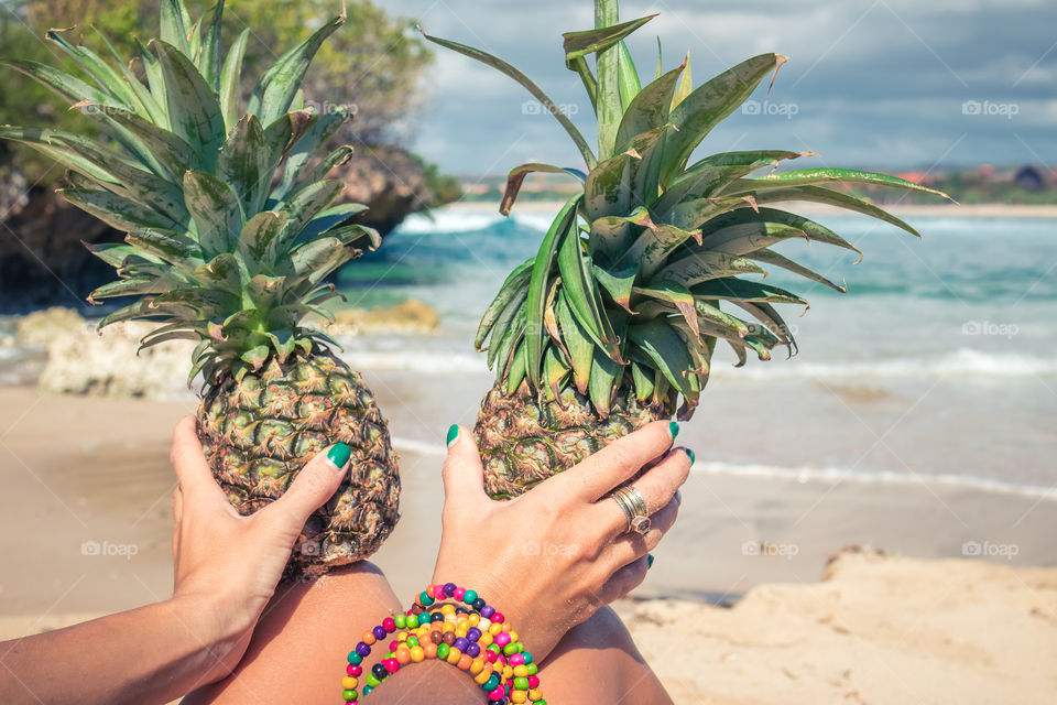 A girl sits on the beach and holds pineapples.