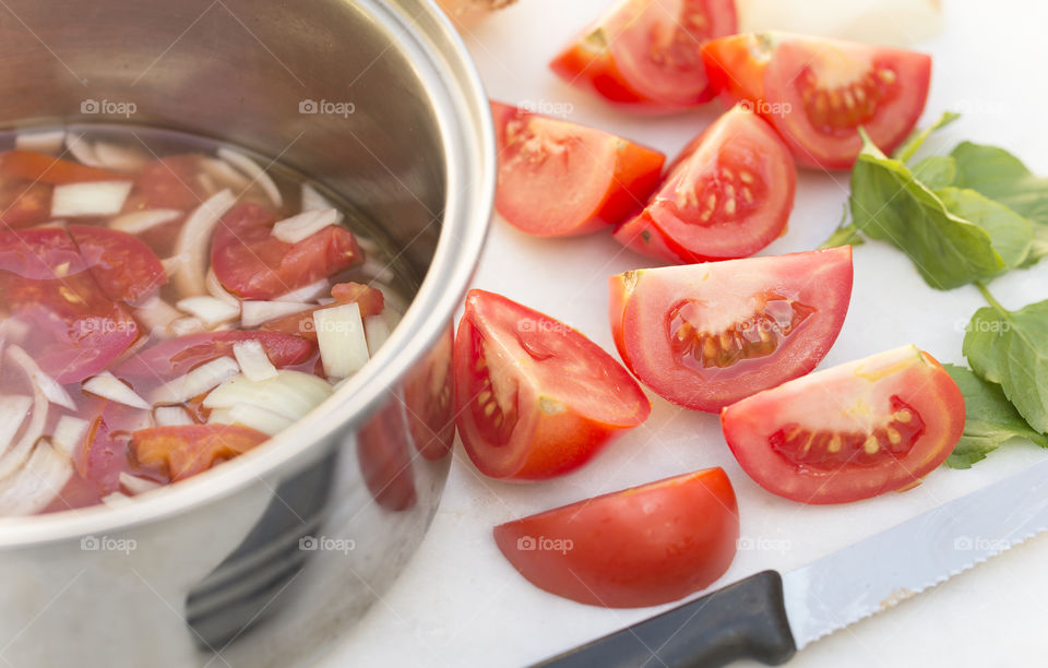 A metal saucepan containing chopped onions and tomatoes with tomato and onion  wedges at the side.
