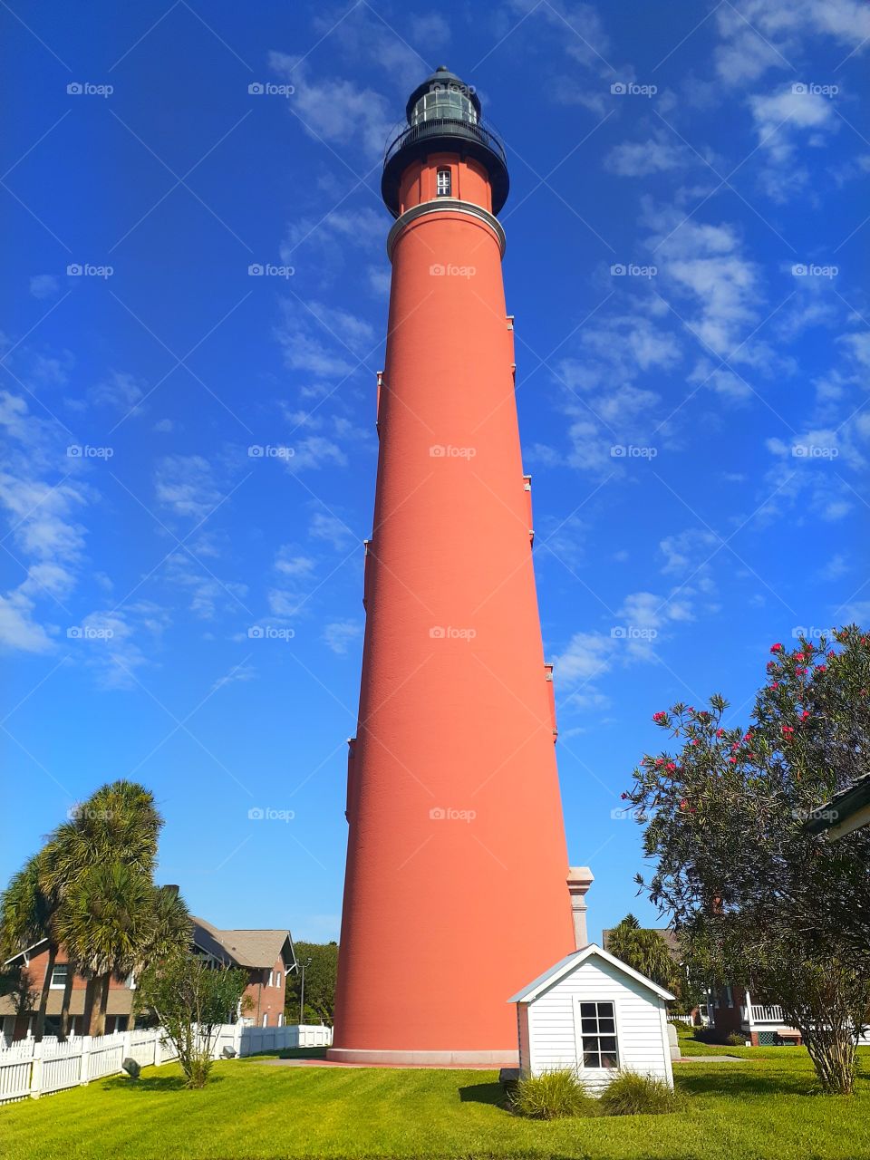 The very tall, red Ponce Inlet lighthouse in Ponce Inlet, Florida against a blue sky.