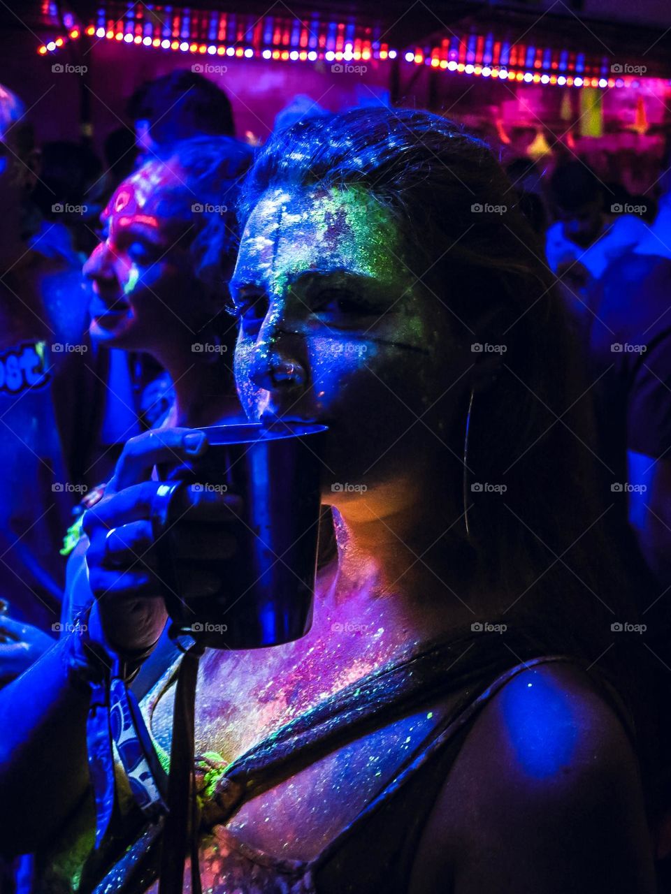 Beautiful Colorful Portrait of a woman with a blacklight and neon colors on the face. Blue Portrait with green and orange neon details. Beautiful Girl Drinking with neon lights