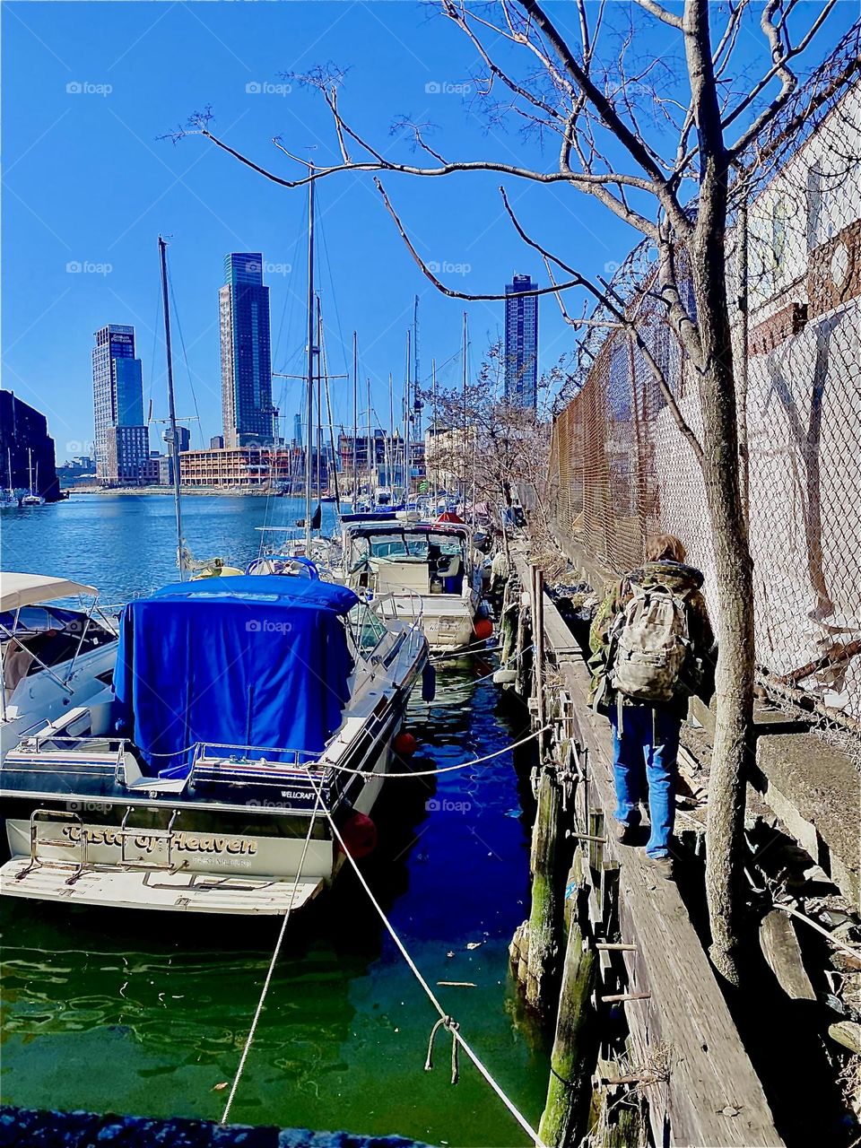 Timothy is walking along the wall by the East River towards our boat, the “Salvation”. It has provided to us just that: Salvation, and a home. In order to get there he has to walk on a wide wooden plank. 2023. Hypnotic Productions