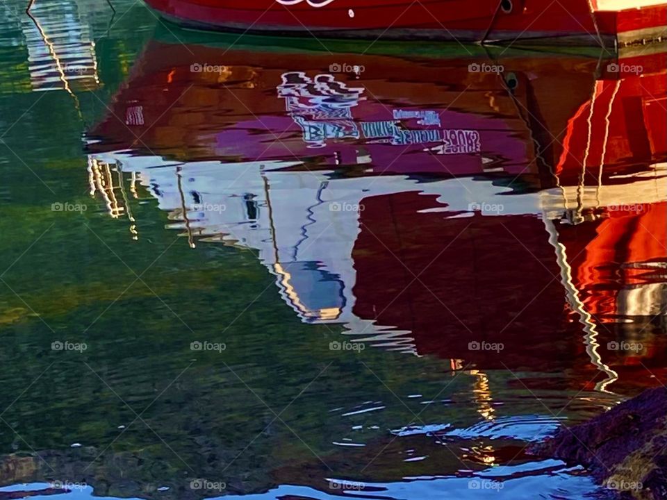A red boat and green mountain reflected in a mirror like sea.