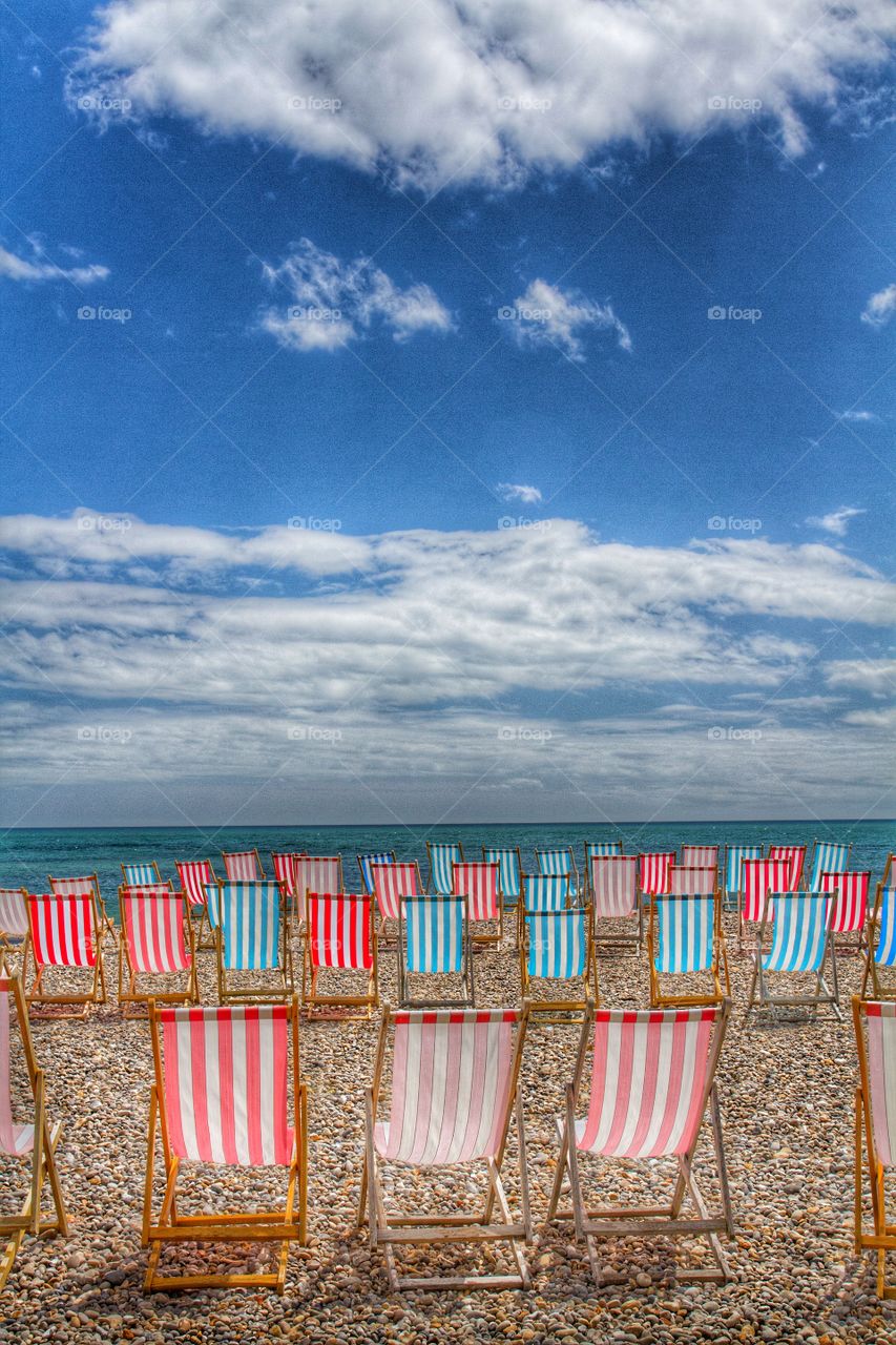 Deckchairs On The Beach. Lots of empty deckchairs on a deserted pebble beach. Beautiful summer's day.