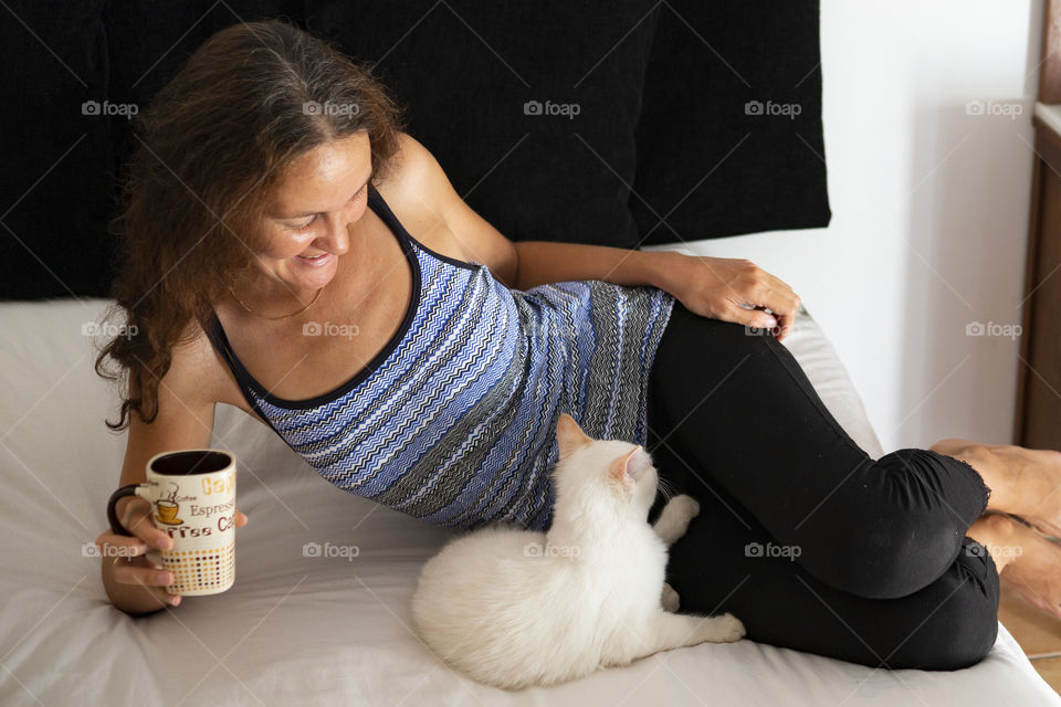 Girl drinks coffee and plays with a cat.