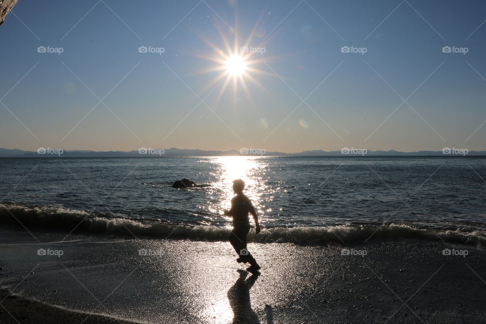 Sun casting its light in the ocean and silhouette of a man reflecting on the enlightened sandy shore