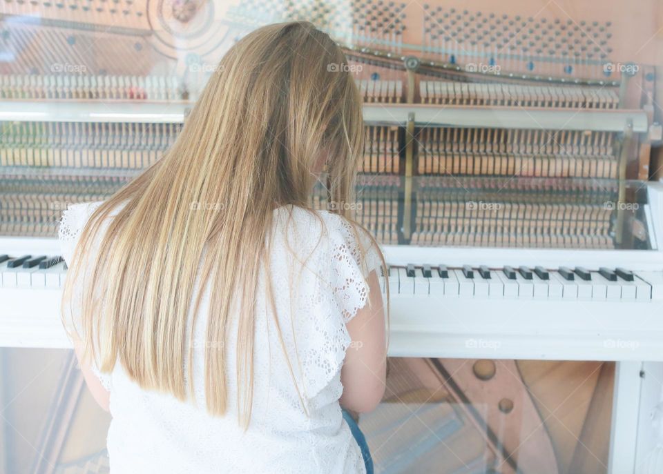 Girl with beautiful hair is sitting by the piano 