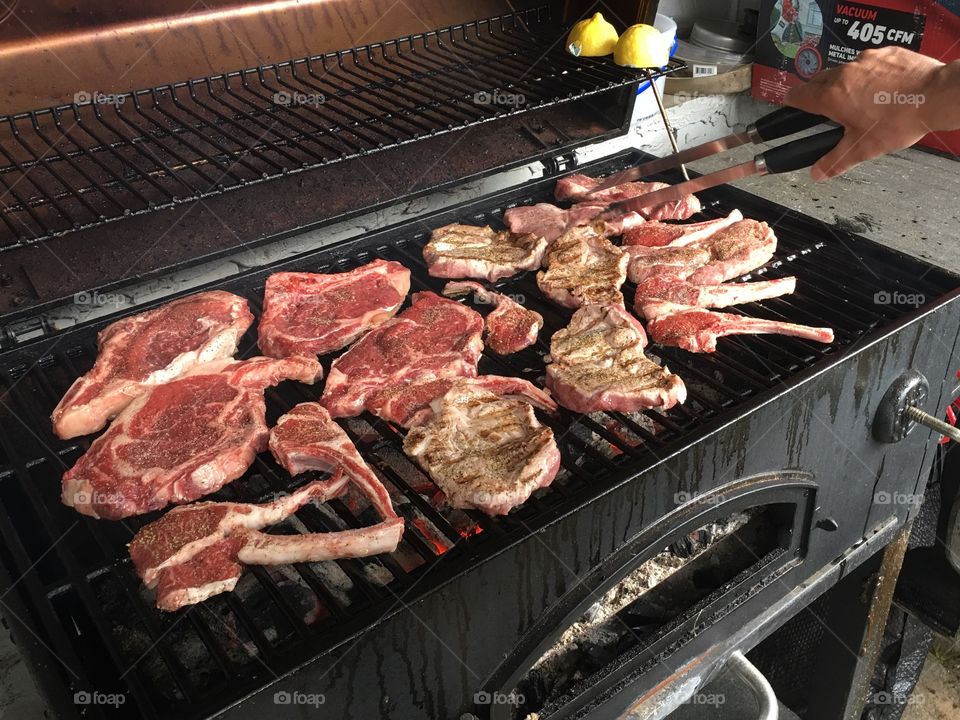 Man’s hand flipping steaks and lamb chops on the barbecue
