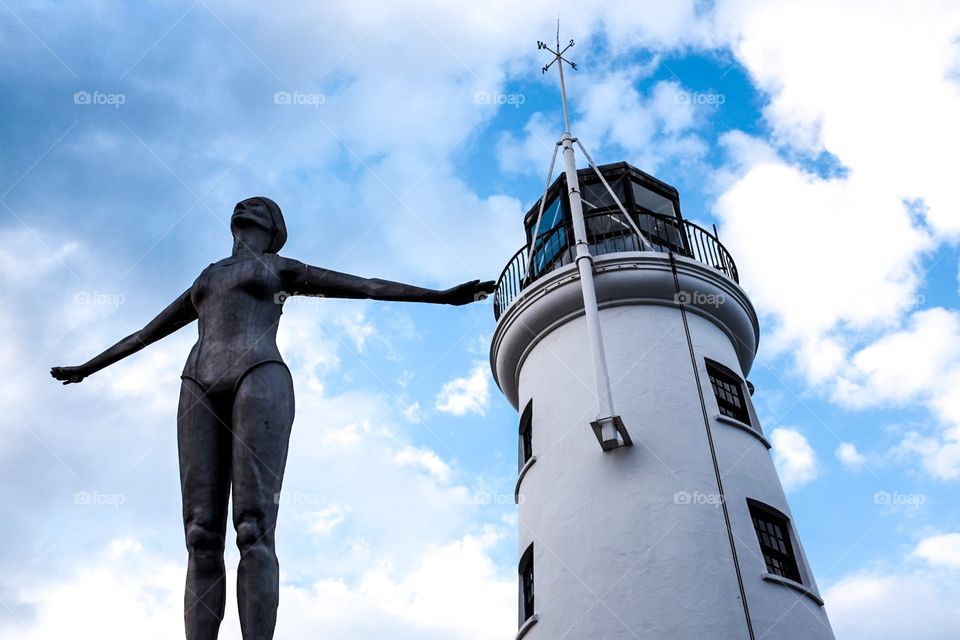The Lighthouse Diver . A statue of a woman in a diving pose stands in front of a white lighthouse in Scarborough, UK. 