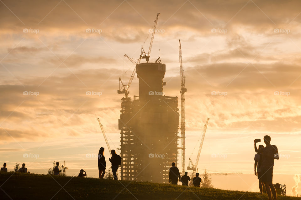 silhouette of a skyscraper under construction and silhouettes of people walking