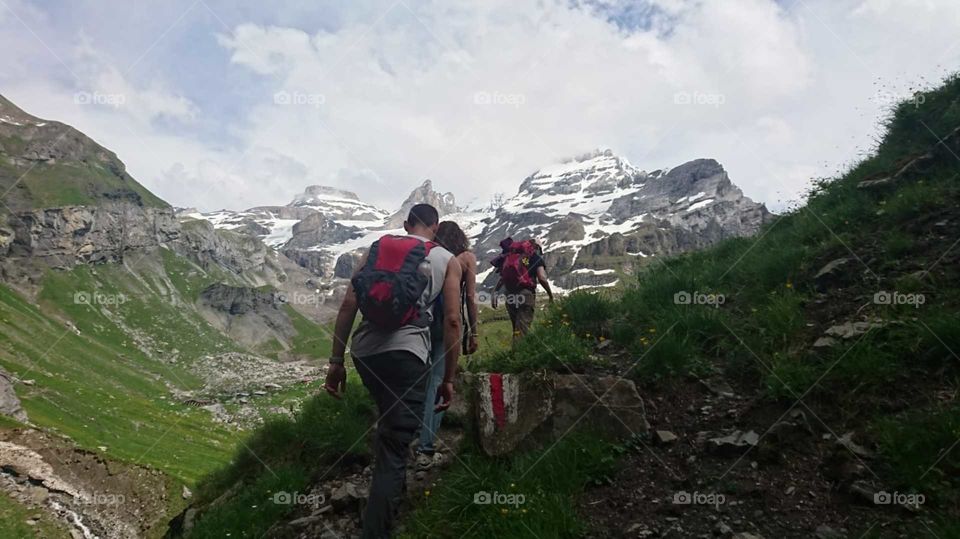 Hiking through the Alpes, sleeveless to cool down, surrounded with snow and green living plants. 