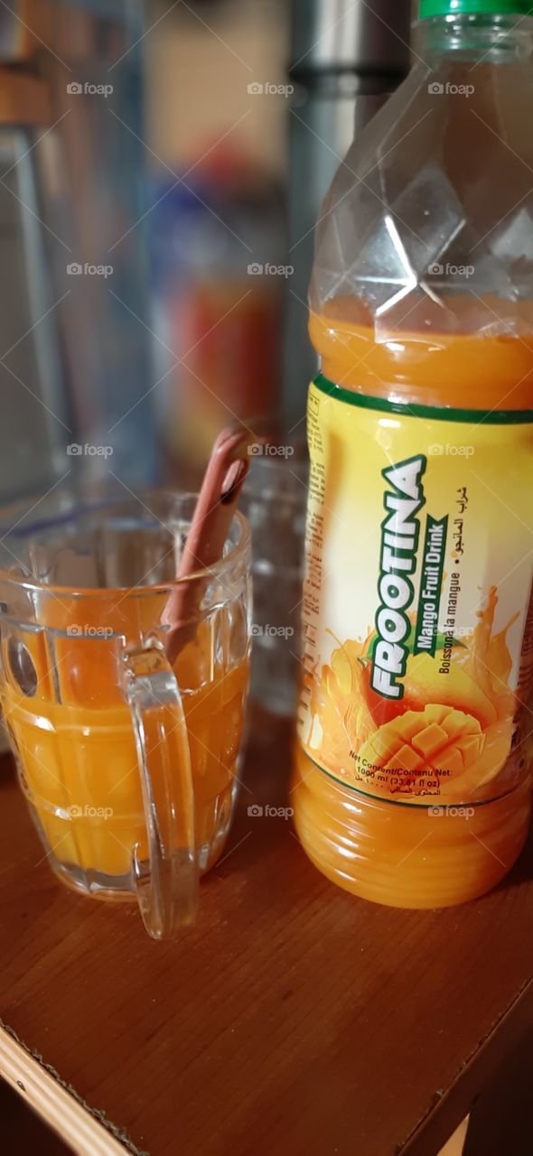 a glass of mango juice, bottle of juice with labelled name...glass of juice with spoon of red handle
