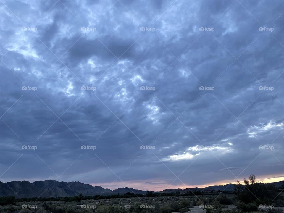 A pink and yellow sunset with dark clouds above and mountains below. 