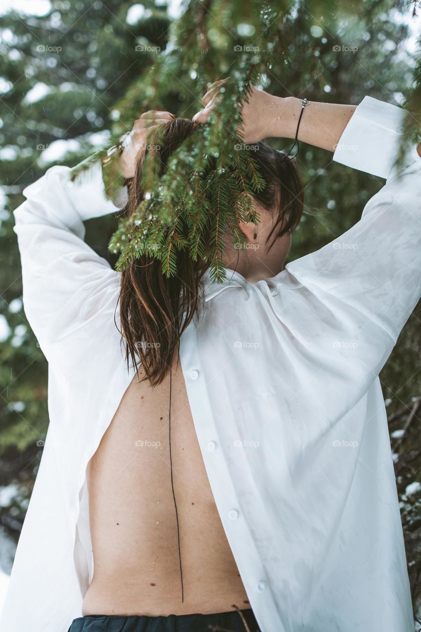 woman tying her hair and revealing her spine tattoo in the woods