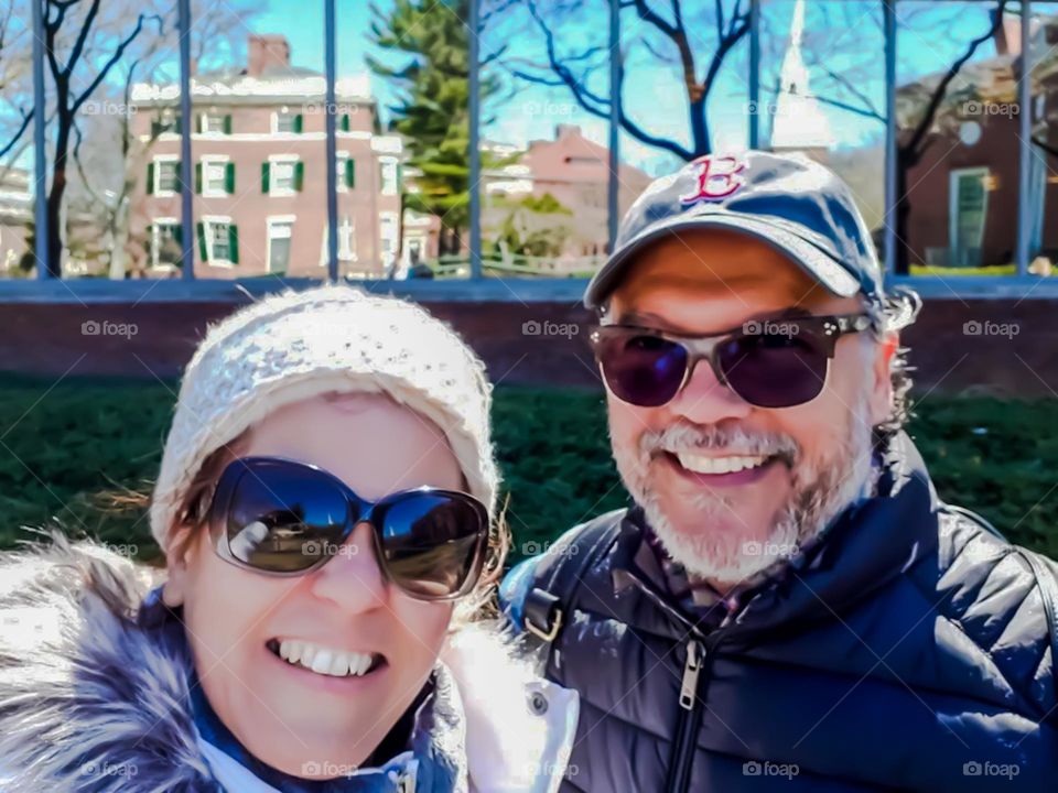 Selfie: Couple with their backs to a glass building reflecting the buildings and landscape in front. Also reflected in the sunglasses.