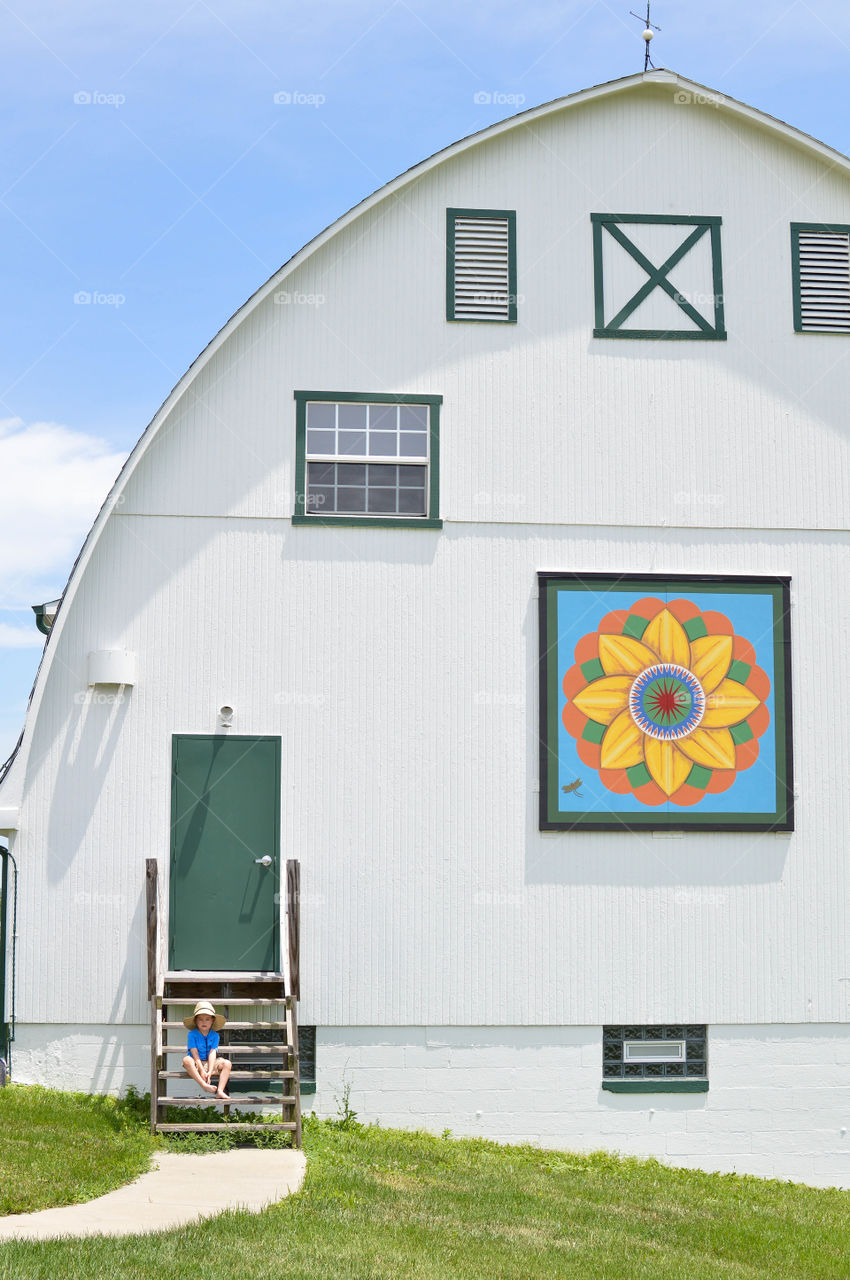 Young boy sitting on the steps of a large barn in the countryside on a bright summer day