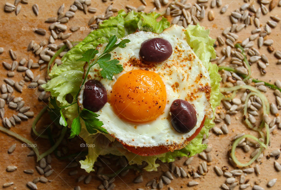 Burger sandwich with an egg, olives, seeds and lettuce