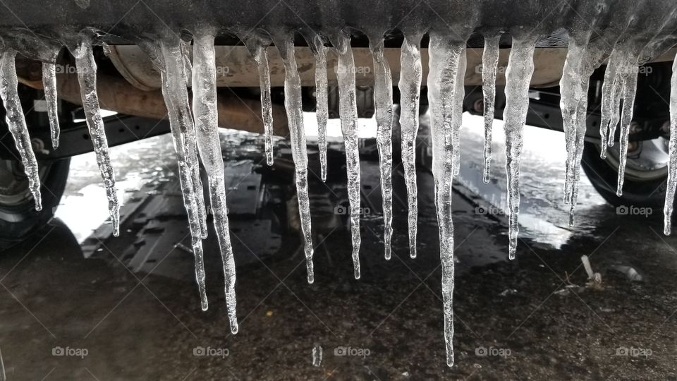 A line of icicles hanging from the rear bumper of a frozen car.