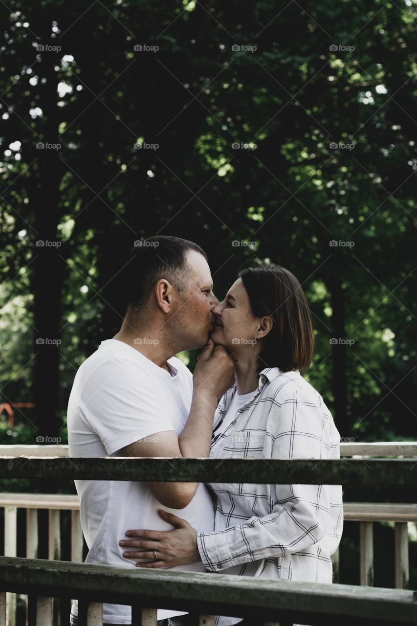 Portrait of one young beautiful Caucasian couple standing on a wooden bridge in a public park and making out on a summer day, close-up side view.