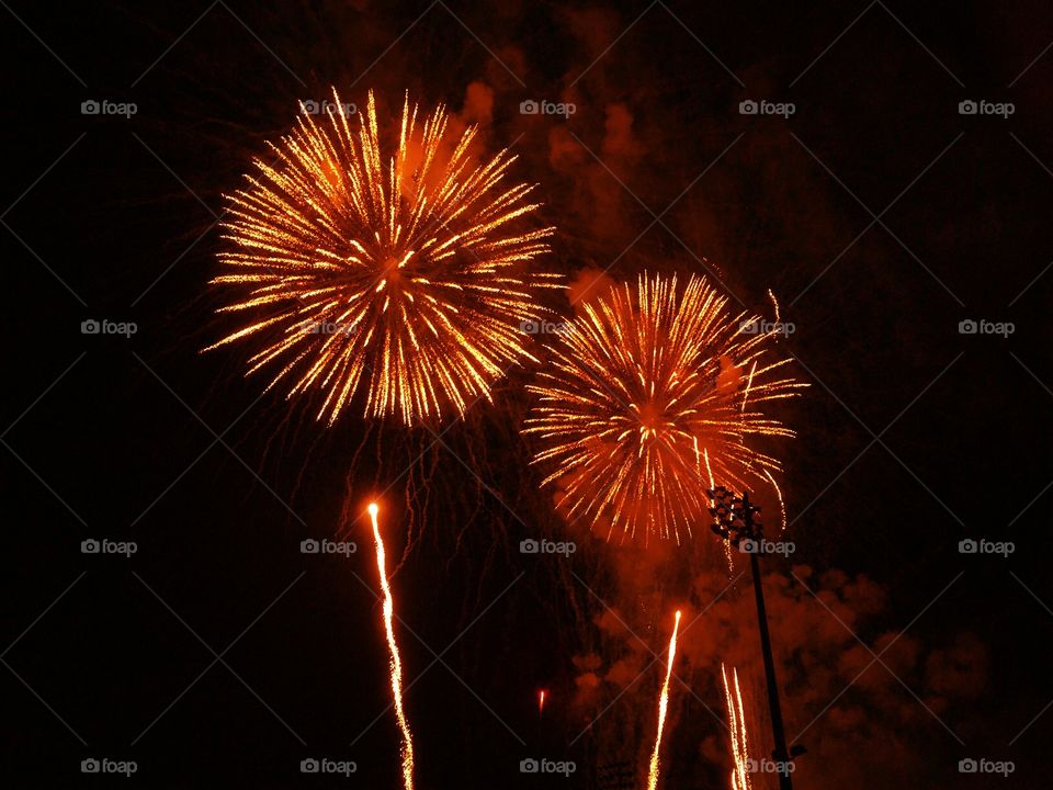 A pair of brilliant orange fireworks dazzle the dark sky.