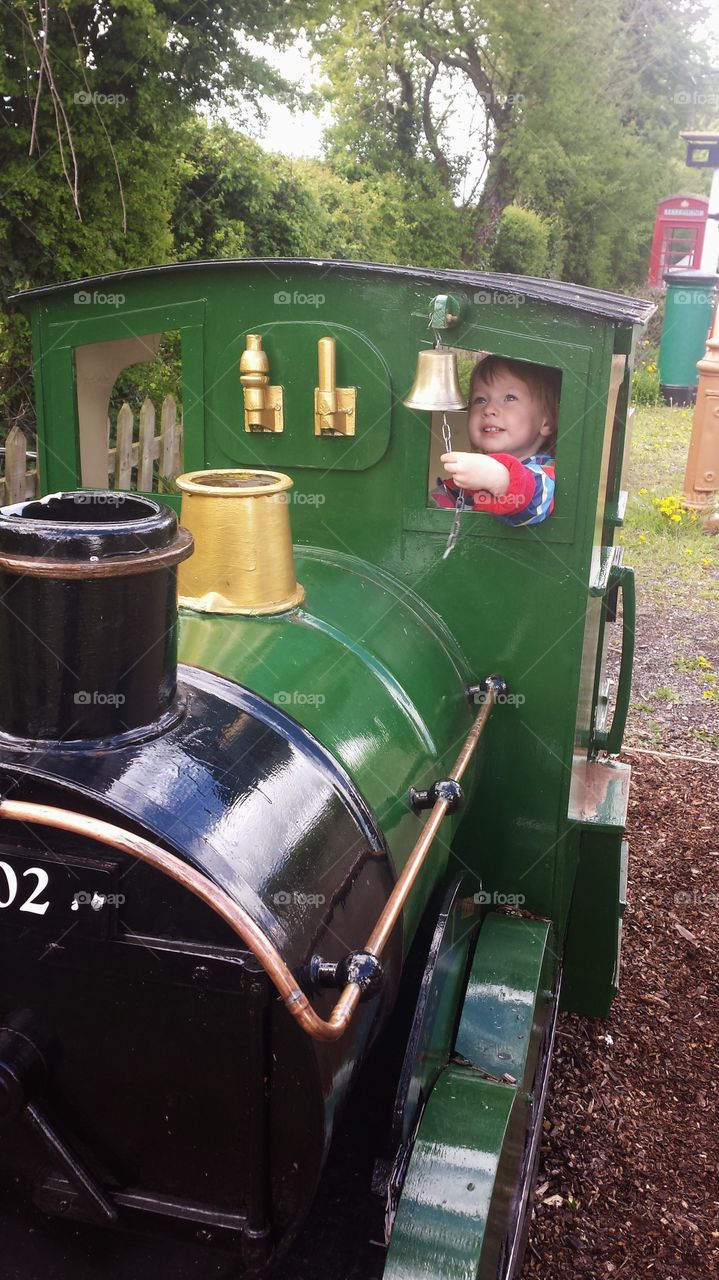 small child in wooden toy train ringing the bell
