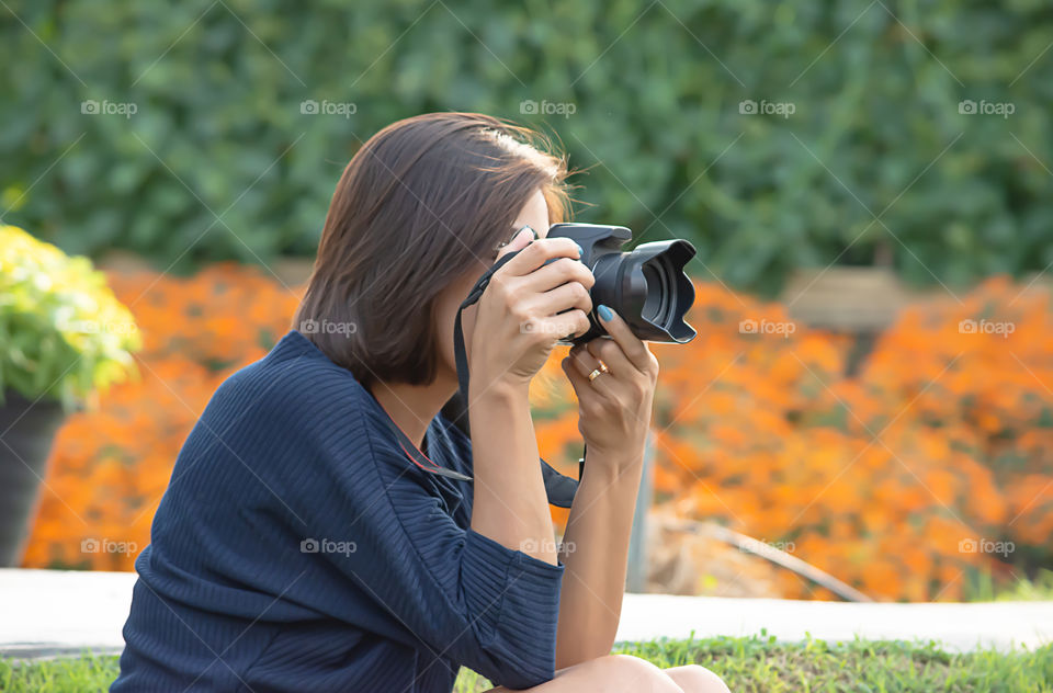 Hand woman holding the camera Taking pictures Background of trees and flowers