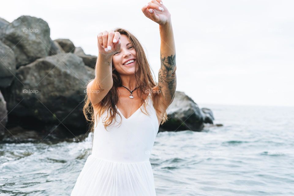 Young carefree beautiful woman with long hair in white dress enjoying life on sea beach