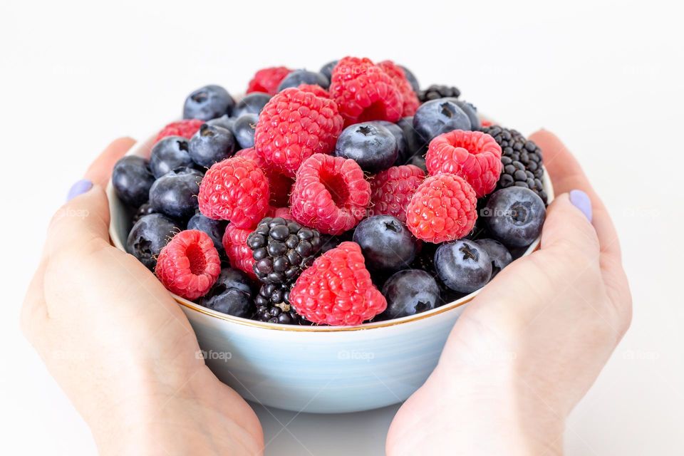 Fresh berries in a bowl in female hands, delicious summer treat