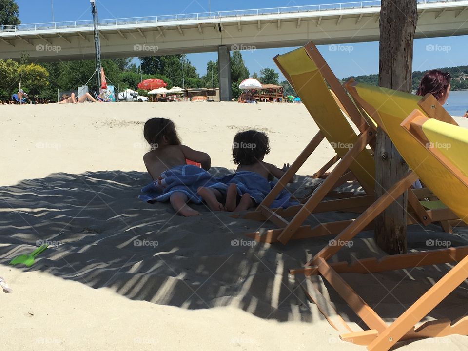 Kids laying in sand in shadow of parasols on the beach