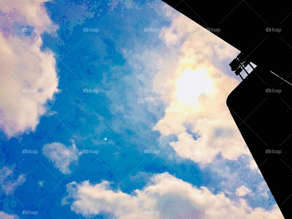 A view up into the blue summer sky of Long Island City, Queens, New York with clouds and a dark silhouetted outlining of two buildings. Photo from 2020. Hypnotic Productions