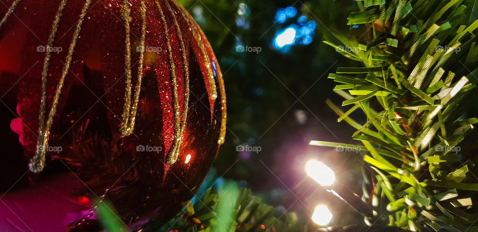 red beautiful christmas ball lit by a christmas light hanging in a fake christmas tree