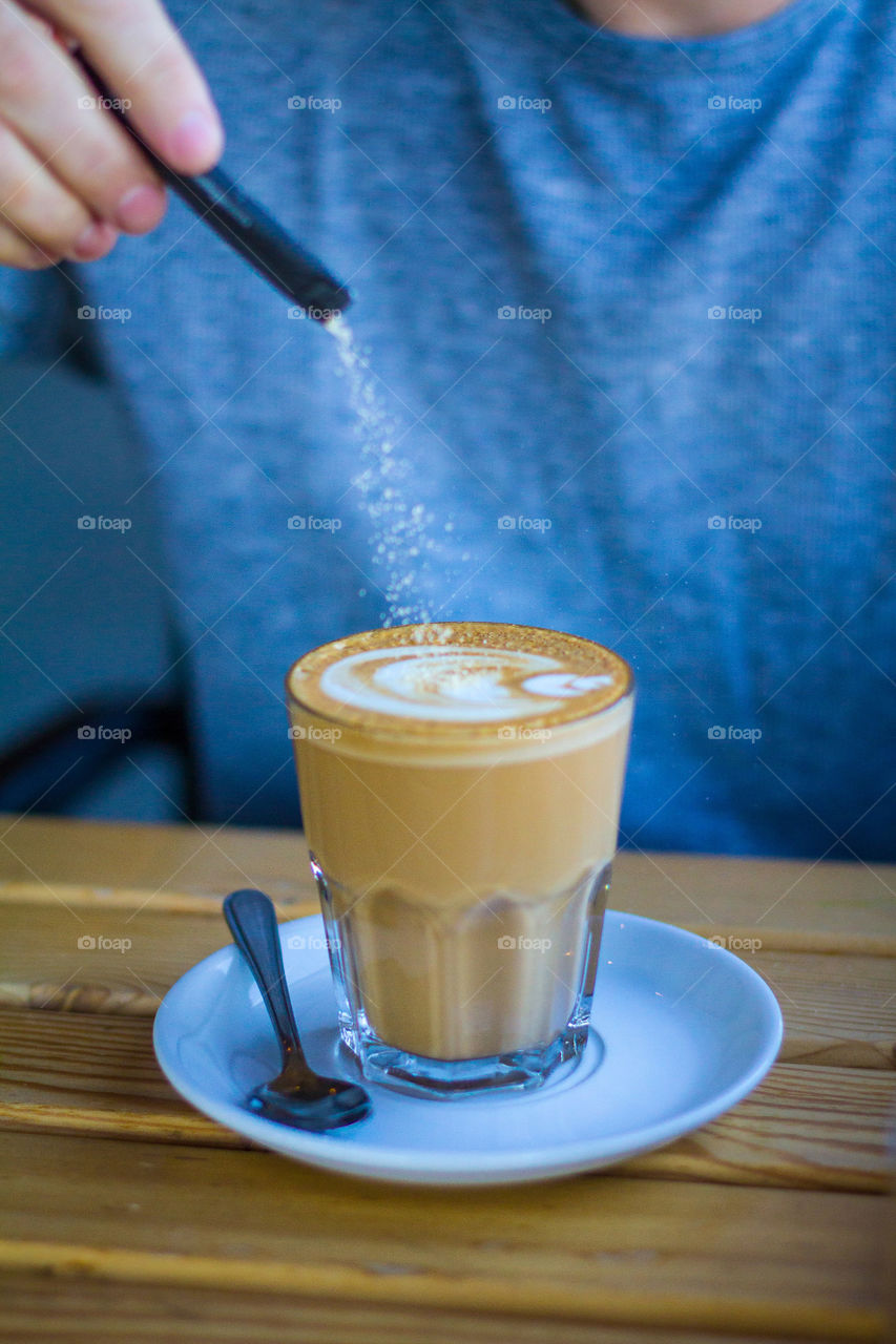 In motion - capturing sugar falling into a cup of coffee with latte art. Image with blue colors and delicious brown coffee in glass cup.