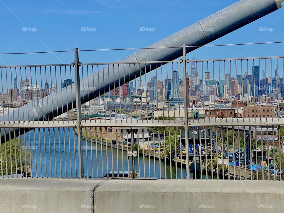 A sideways bar of the „Kosciuszku Bridge“ which is a modern drawstring bridge spanning the E River at „Newtown Creek“ from LIC, Queens into Brooklyn, NY. The East River is visible below and Manhattan in the far distance. 2022. Hypnotic Productions
