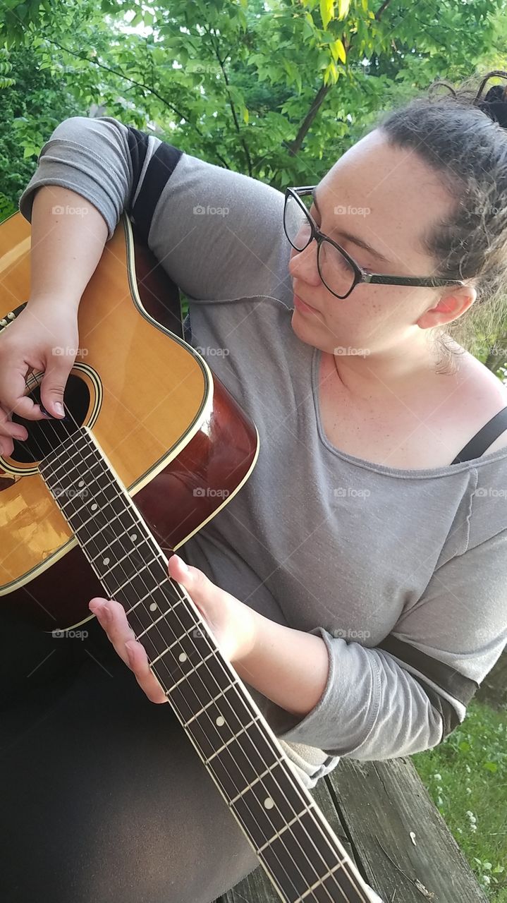 pretty teenager playing guitar, tuning it, sunny pretty and shiny, glasses long sleeve