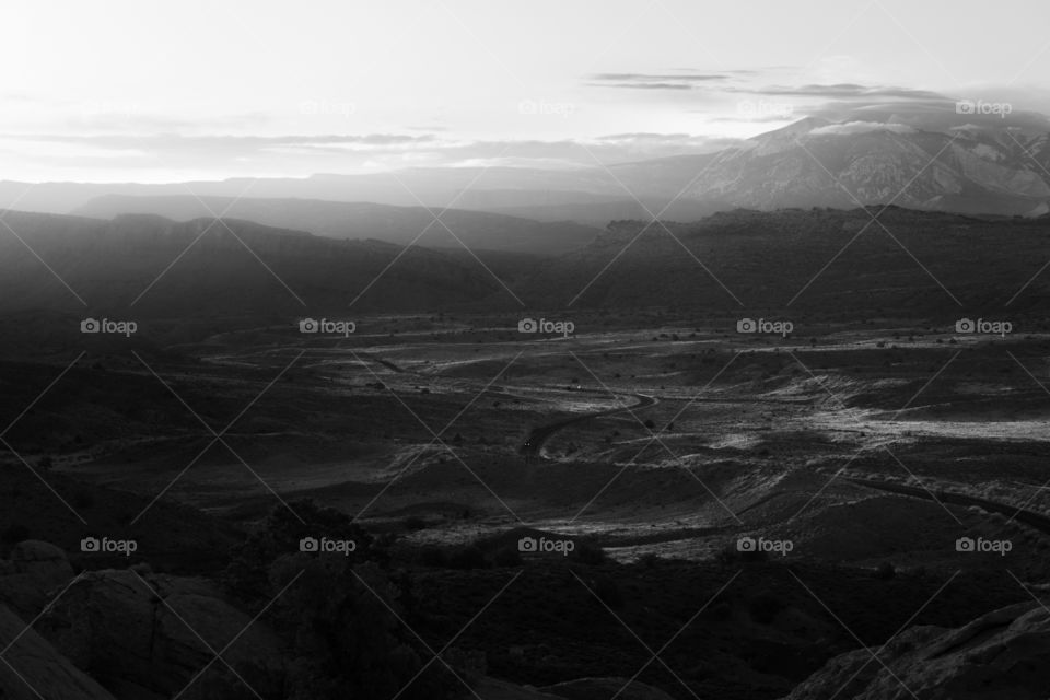 A hazy sunrise lights up a valley in Arches National Park in Moab, Utah with mountains in the background.