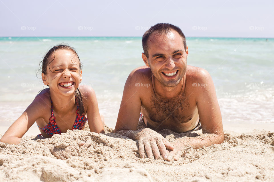 Laughing father and daughter on sandy beach 