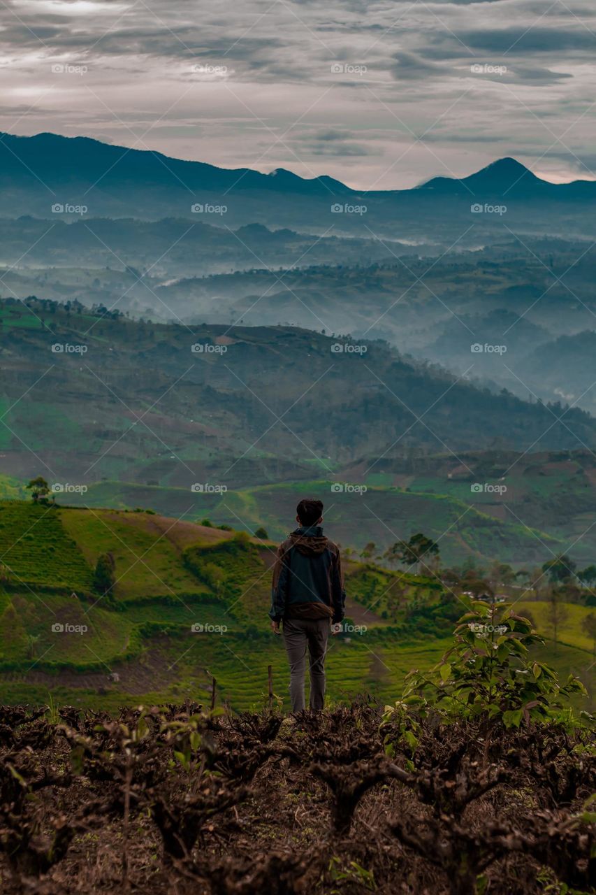 man standing facing the view of the hills in the morning covered in light fog
