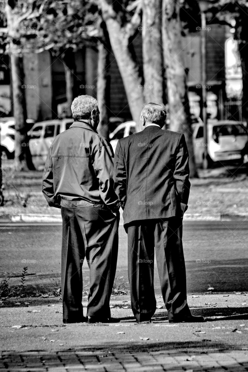 a pair of old men talk standing on the sidewalk