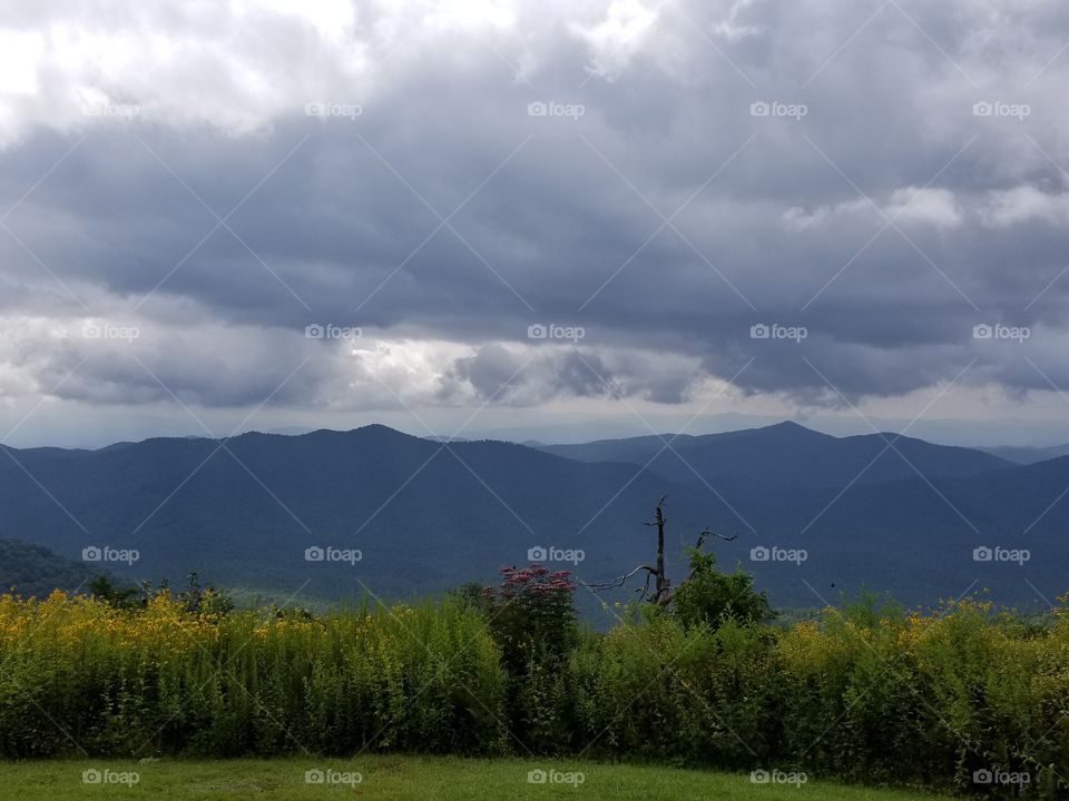 Clouds over the mountaintops and a field of grass.