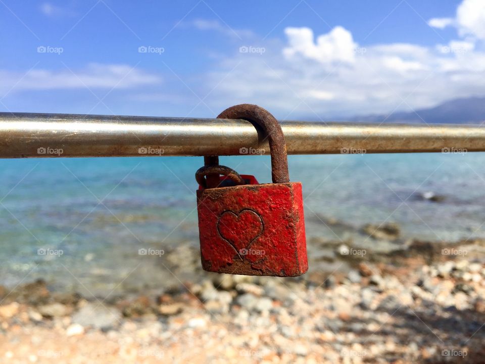 Red padlock with heart on it on a bridge over the sea