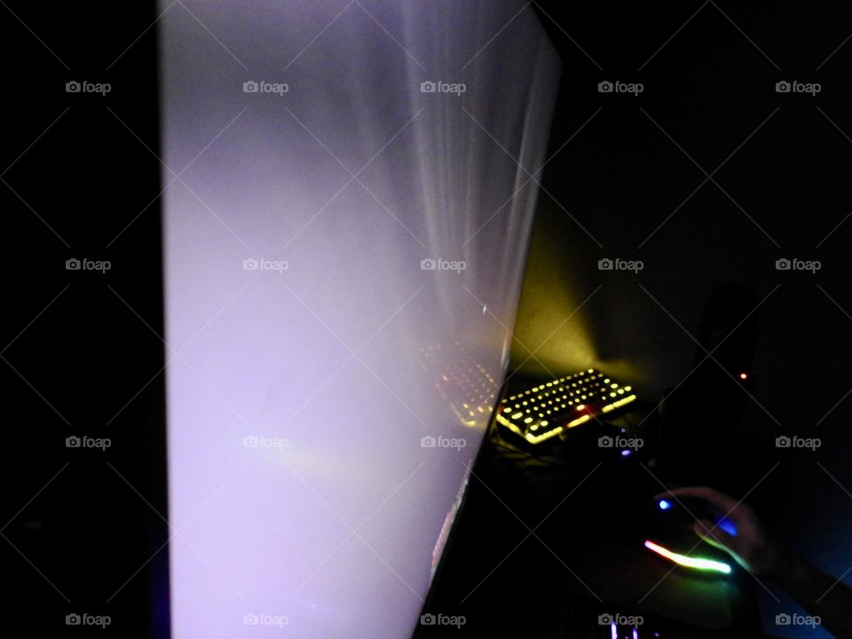 Teenager boy playing Minecraft on the gaming computer seen from his left side and close-up of his hand playing in a dark room and macro effect on the screen.