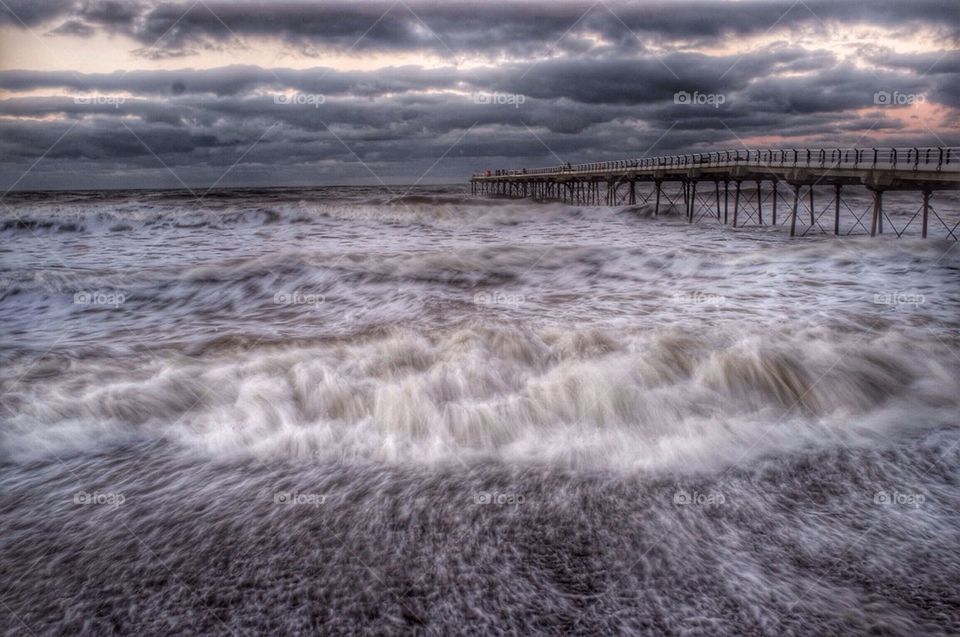 The sea swirls around a pier before rushing on to the shore in this