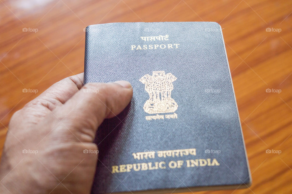 Man holding Indian Passport book over wooden table hardwood floor background, selective focus. Close up. Travel tourism and holiday vacation concept. Copy space room for text.