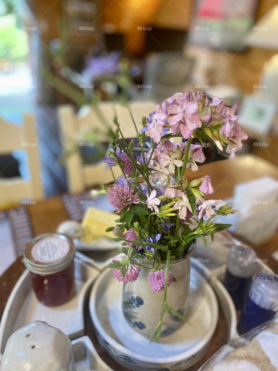 This image shows a lovely bouquet of wildflowers arranged in a ceramic vase with a blue floral design. The flowers are a mix of purple, pink, and blue hues, adding a vibrant and natural touch to the indoor cottage setting. 