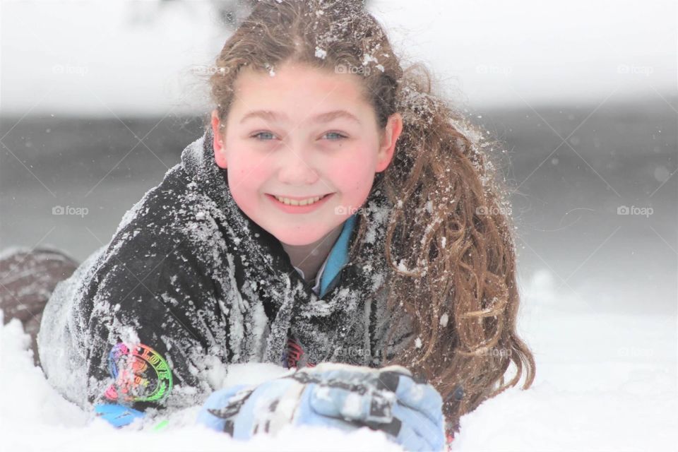 This beautiful little blue-eyed girl taking a moment to smile while enjoying her time in the fluffy white snow of winter. 