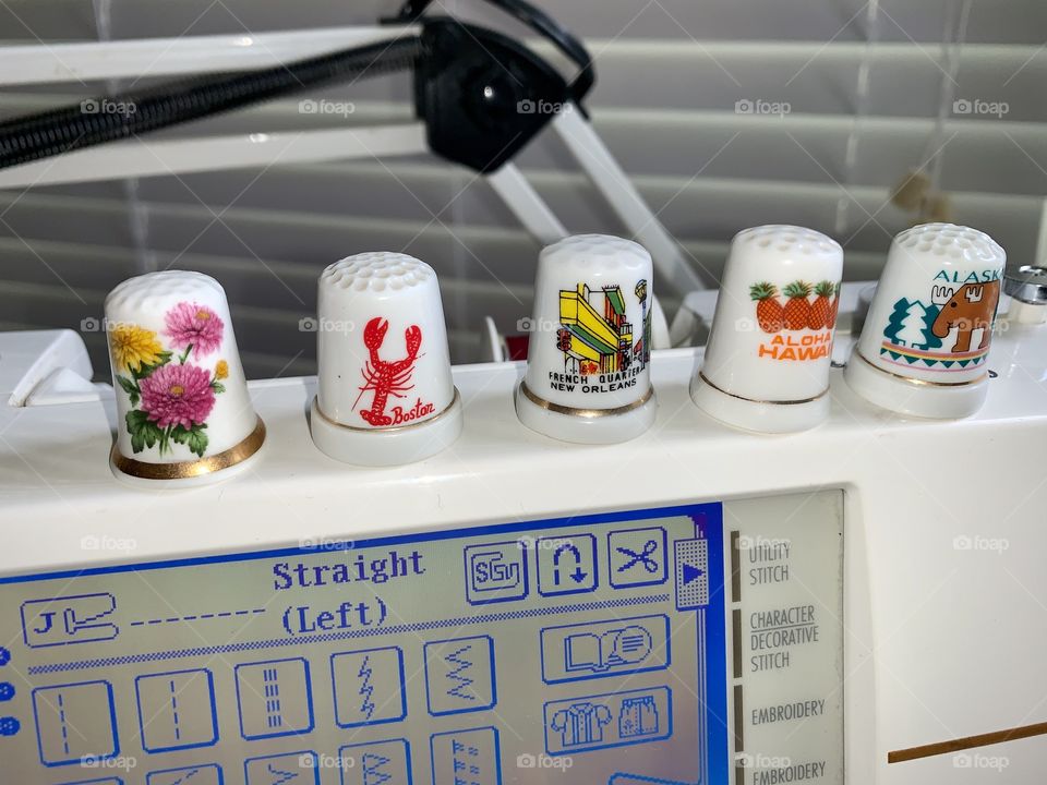 T - Decorative thimbles from different states. A thimble is a small hard pitted cup worn for protection on the finger that pushes the needle in sewing.
