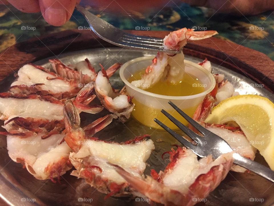 Using a fork to dip broiled rock shrimp tails from a platter into melted butter at a seafood restaurant 
