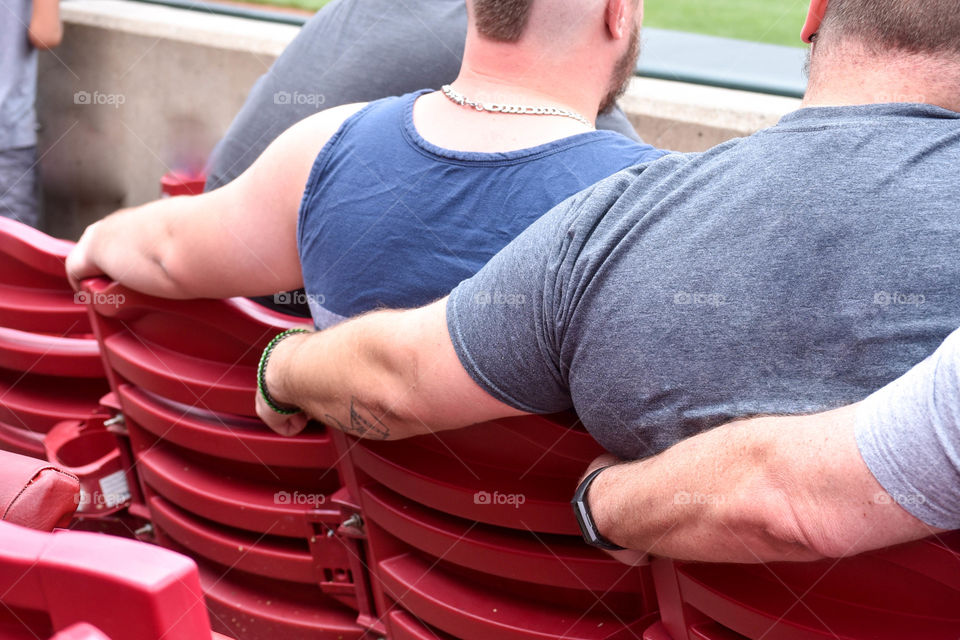 Back view of three people sitting in stadium seats, each with an arm around the next person