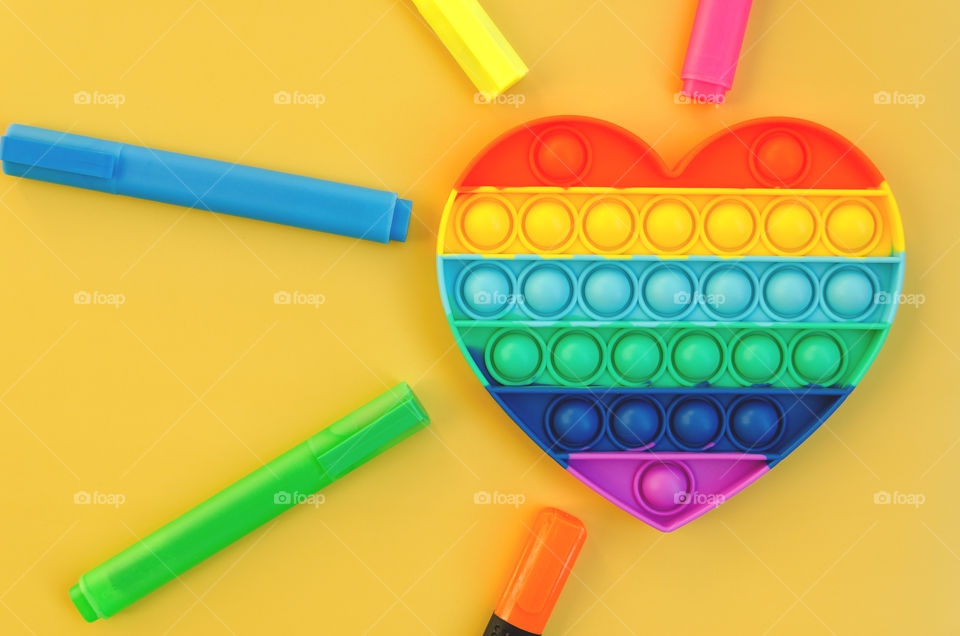 Top view of anti stress sensory toy Pop it rainbow heart on yellow background. Popular, trend toys in 2021