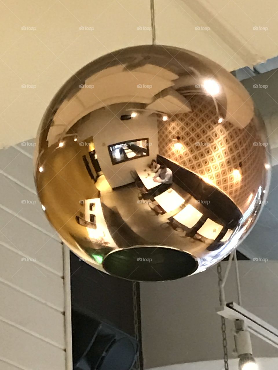 Reflection caught in spherical gold lighting fixture at cozy cafe